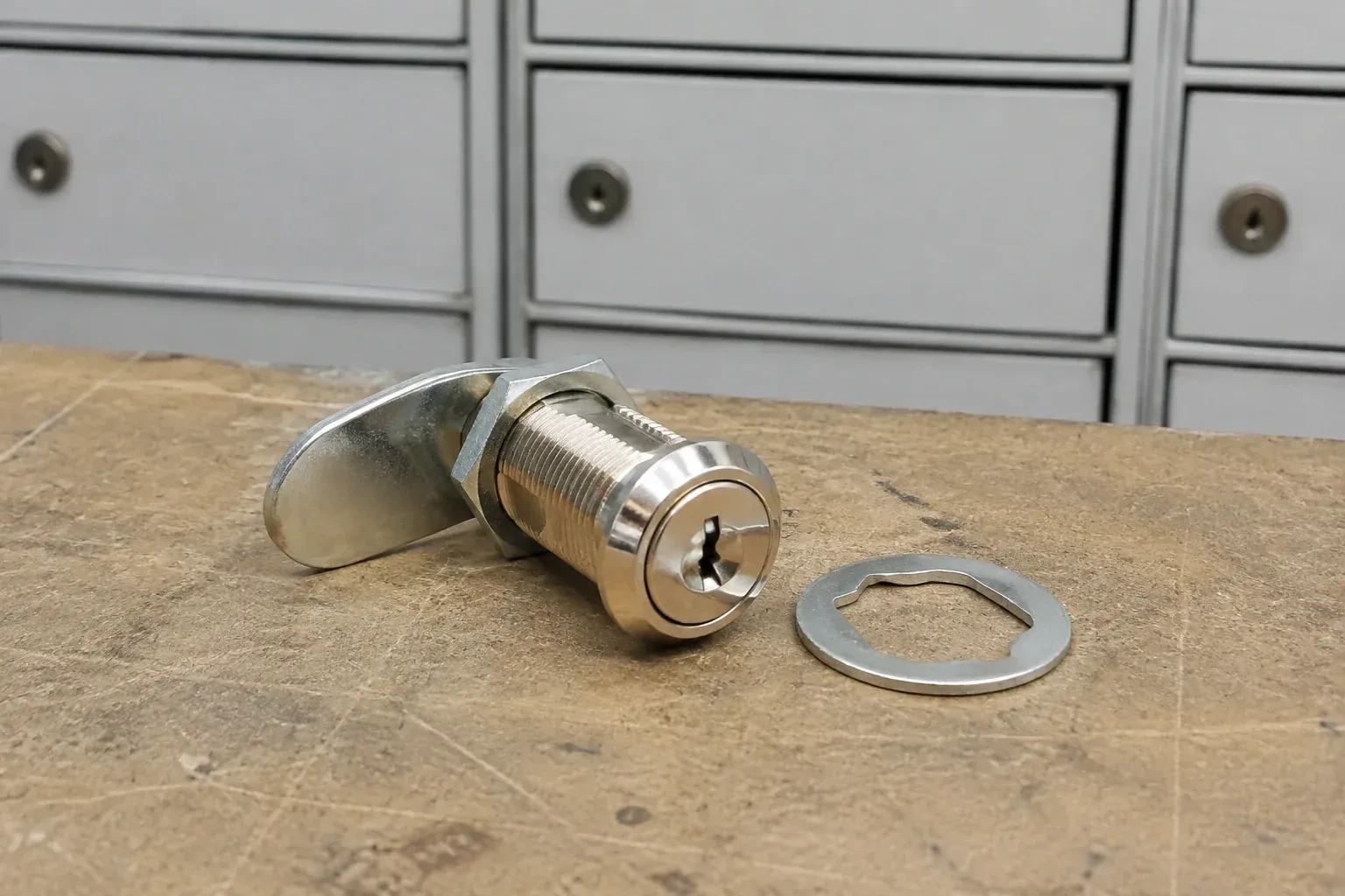 Detached threaded cam lock and mounting washer on a workbench in front of closed mail compartments. — Mailbox Lock Replacement, Cobourg